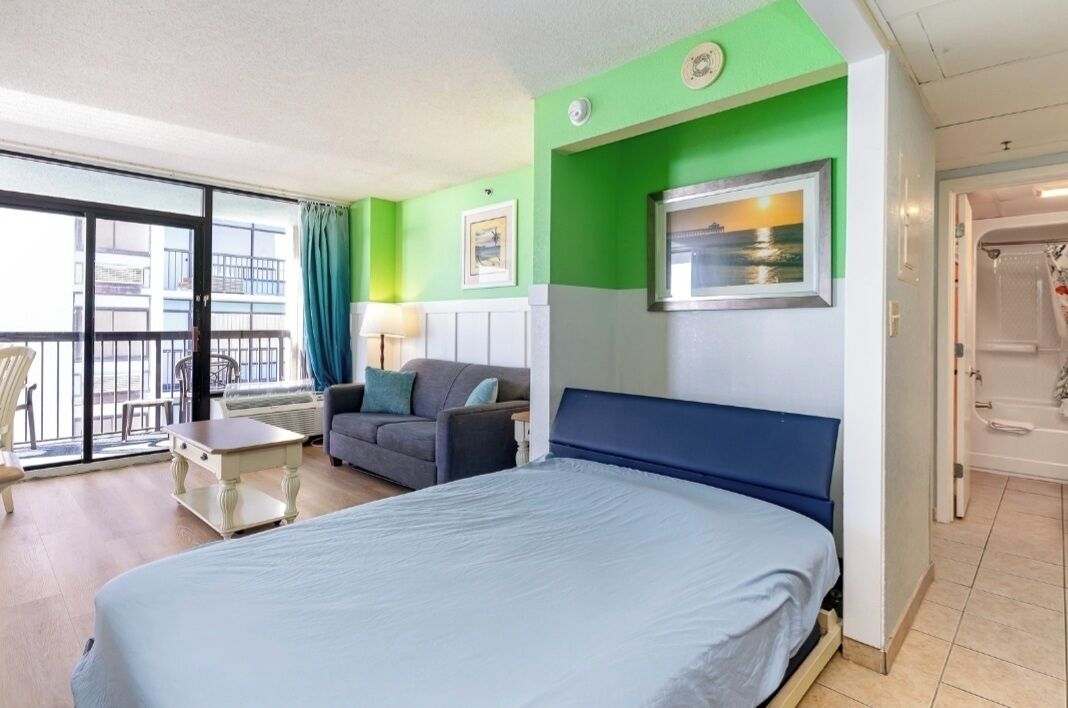 A hotel room with a bed, a sofa, a small table, and a window with a view of the outside.