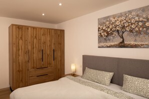 A bedroom with a large wooden wardrobe, a bed with patterned pillows, and a wall painting of a tree. - Kraichgaublick Ground-Floor Apartment (Epfenbach)