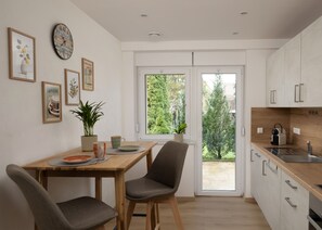 A modern kitchen with white cabinets, a wooden countertop, and a dining area with two chairs and a table. - Kraichgaublick Ground-Floor Apartment (Epfenbach)