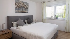 Un dormitorio con una cama grande, una mesita de noche, una lámpara, una ventana con cortinas y un cuadro en la pared.
