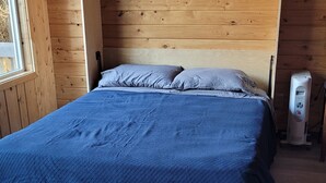 A wooden-paneled room with a bed, a window, and a heater. - Remote Alaska cabin, located in the Kachemak Bay Park area of Tutka Bay. (Seldovia)