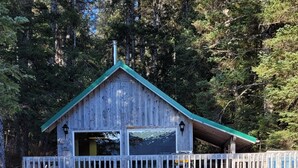 A wooden cabin with a green roof, a balcony, and a staircase leading up to it. - Remote Alaska cabin, located in the Kachemak Bay Park area of Tutka Bay. (Seldovia)