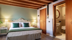 A bedroom with a wooden ceiling, a bed with green pillows, a nightstand, and a bathroom visible through an open door. - v-nice rooms (Venice)