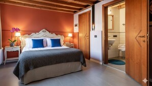 A bedroom with a wooden ceiling, a bed with a white headboard, two bedside tables with lamps, and a nightstand with a plant. - v-nice rooms (Venice)