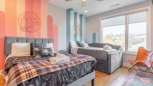 Een slaapkamer met een bed, een bank, een stoel, een plafondventilator en een groot raam.