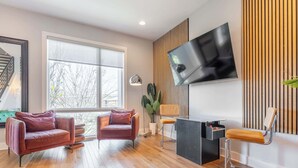 Een moderne woonkamer met een groot raam, twee leren banken, een houten vloer, een zwart bureau en een hangende televisie.