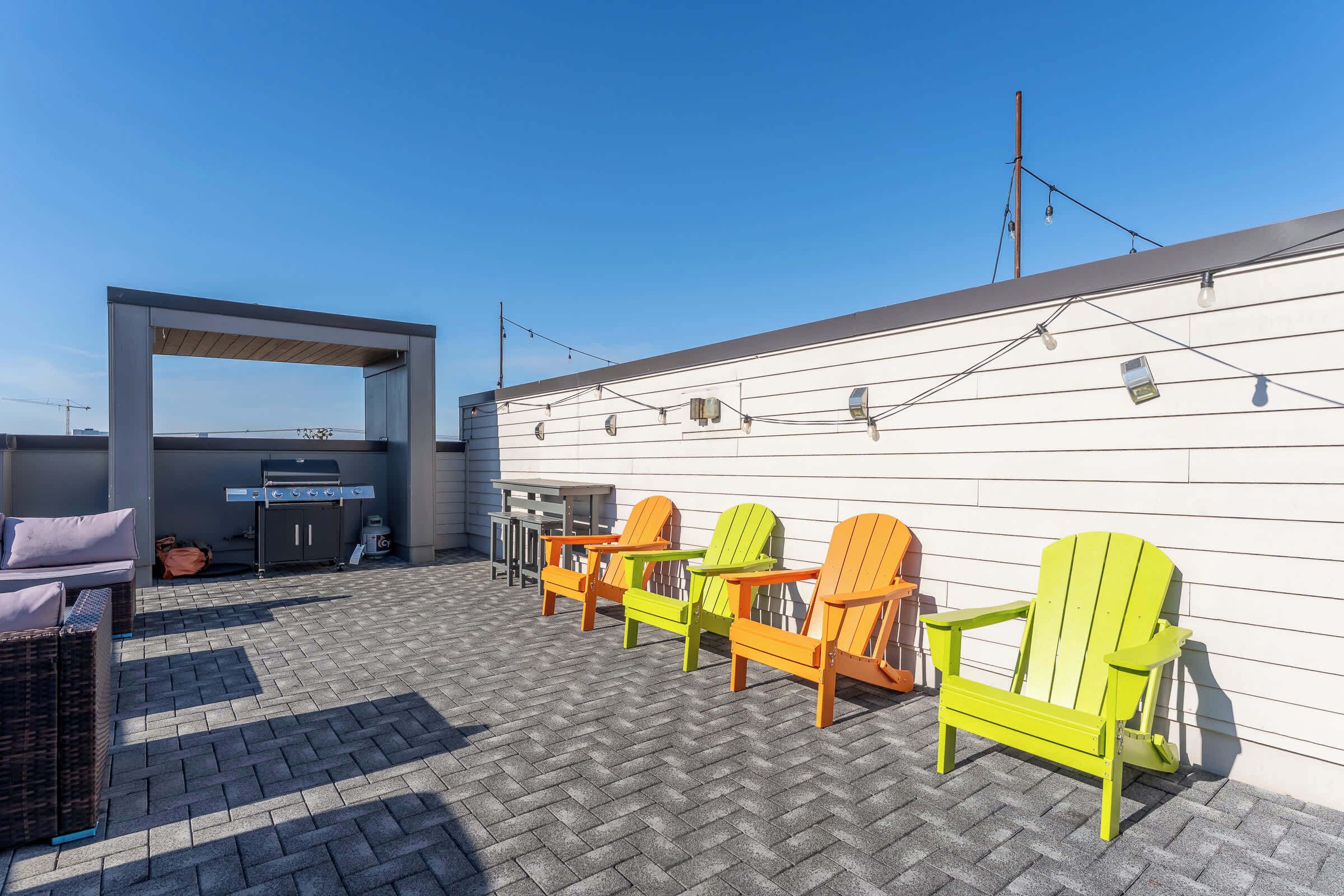Une terrasse sur le toit avec des fauteuils Adirondack, un barbecue et un canapé en osier.