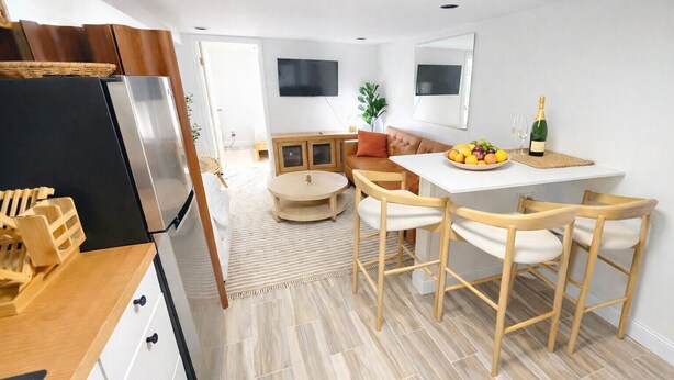 Una cocina moderna con refrigerador empotrado, sillas de madera, una mesa de comedor y un frutero.