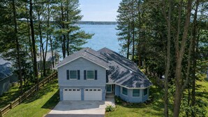 A two-story house with a garage, surrounded by trees and a lake. - Long Lake Haven | 4BR | Waterfront | Boat Rental (Traverse City)