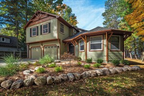 A two-story house with a garage, a small porch, and a stone border around the yard. - Long Lake Haven | 4BR | Waterfront | Boat Rental (Traverse City)