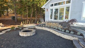 A landscaped garden with a stone fire pit, stone retaining walls, and a variety of shrubs and small trees. - Long Lake Haven | 4BR | Waterfront | Boat Rental (Traverse City)