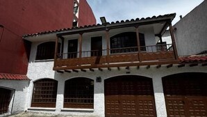 Un edificio de dos plantas con un balcón, varios portones de garaje y un patio empedrado con piedra.