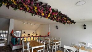 Un comedor con sillas blancas y mesas de madera, suelo de piedra y un arreglo floral decorativo en el techo.