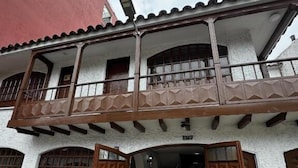 Un edificio de dos plantas con un balcón, grandes puertas de madera y un acceso empedrado con piedras.