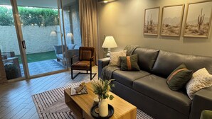 Ein modernes Wohnzimmer mit einer Couch, einem Couchtisch und einem Sessel. Eine Glastür führt in einen Außenbereich.