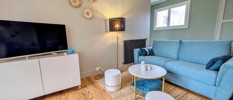 Uma sala de estar moderna com televisão de tela plana, um sofá azul, uma mesa de centro branca e um abajur.