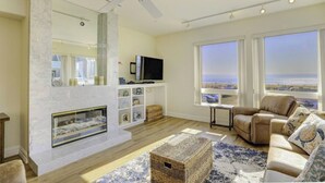 Ein Wohnzimmer mit Kamin, Fernseher und Meerblick.