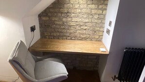 Una habitación pequeña y moderna con techo inclinado, un escritorio de madera, una silla de oficina gris y un radiador.