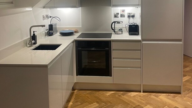 Una cocina moderna con armarios blancos, horno empotrado, fregadero y refrigerador.