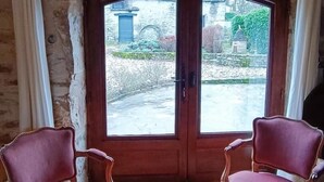 Una habitación con pared de piedra, puerta de madera con paneles de vidrio y dos sillones tapizados en rojo.