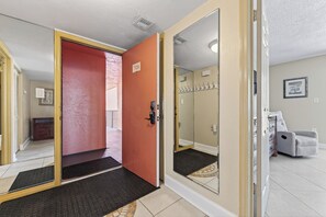 Un pasillo de hotel con una puerta roja, un espejo y un sillón gris.