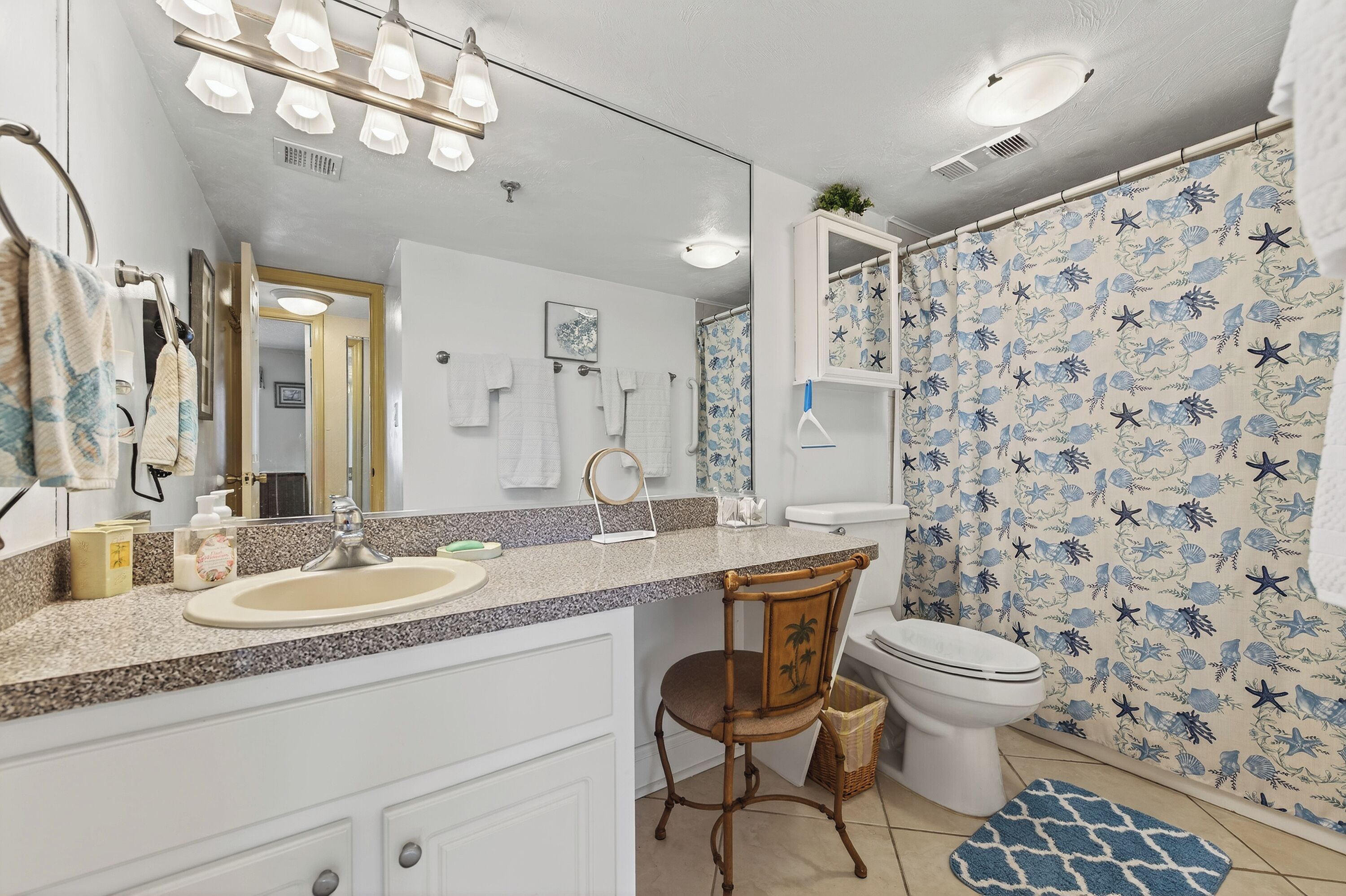 A bathroom with a sink, mirror, and toilet. There is a chair and a shower curtain with a starfish pattern.