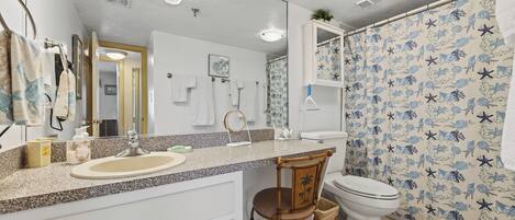 A bathroom with a sink, mirror, and toilet. There is a chair and a shower curtain with a starfish pattern.