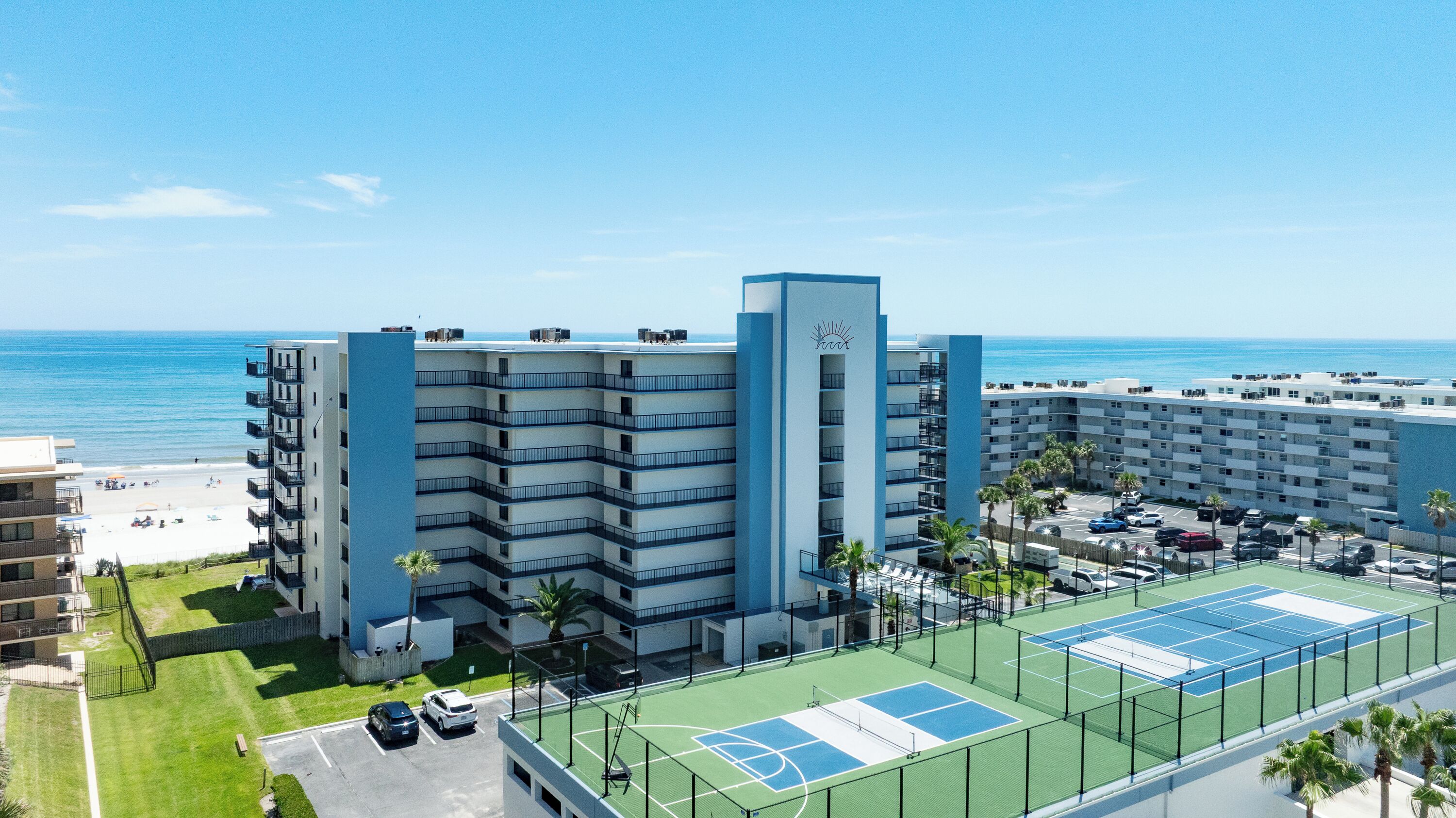 A multi-story hotel with a beach view, tennis courts, and a parking area.