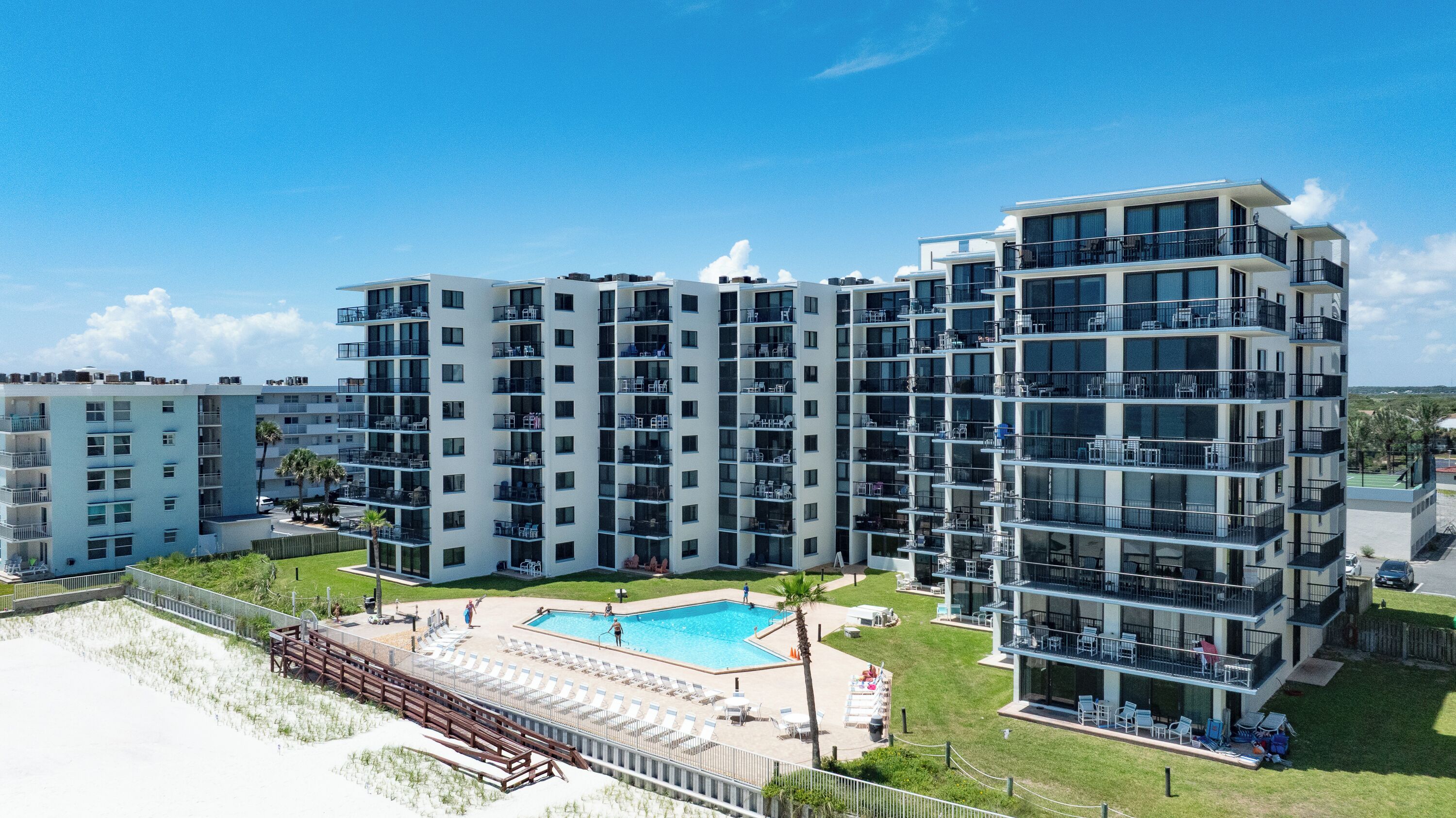 Un immeuble résidentiel à plusieurs étages doté de balcons, d’une piscine et d’un espace aménagé en plage.