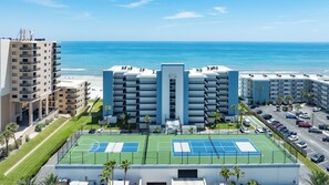 A multi-story hotel with a tennis court, a pool, and a view of the beach. - Stunning Oceanfront 3-Bedroom, 2-Bath Condo – Breathtaking Views! (New Smyrna Beach)