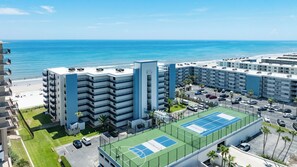 A multi-story hotel with a tennis court and a beach view. - Oceanfront Bliss – 2BR/2BA Condo with Stunning Views @ Sunrise (New Smyrna Beach)