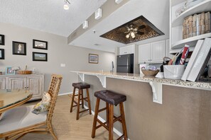 Una cocina moderna con una isla central, taburetes de bar y un comedor con mesa y sillas.
