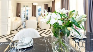 A modern hotel room with a marble dining table set for a meal, a plush sofa, and a large window with curtains.