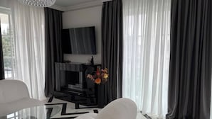 A modern living room with a glass coffee table, white armchairs, a black entertainment unit, and a fireplace.