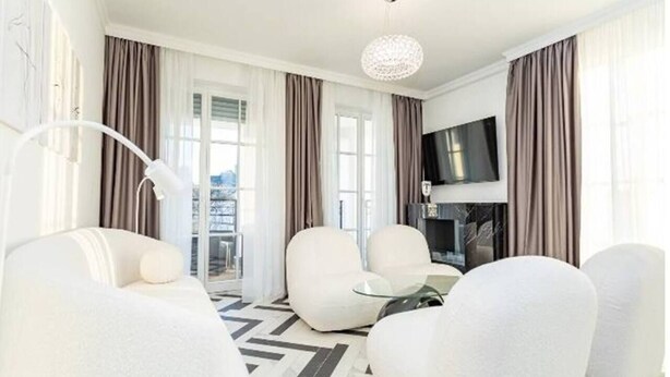 Un salon moderne avec des canapés blancs, une table basse en verre et un téléviseur à écran plat fixé au mur.