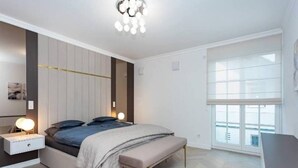 Een moderne slaapkamer met een bed, nachtkastjes, een bankje en een groot raam.