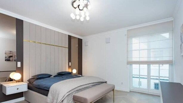 A modern bedroom with a bed, bedside tables, a bench, and a large window.