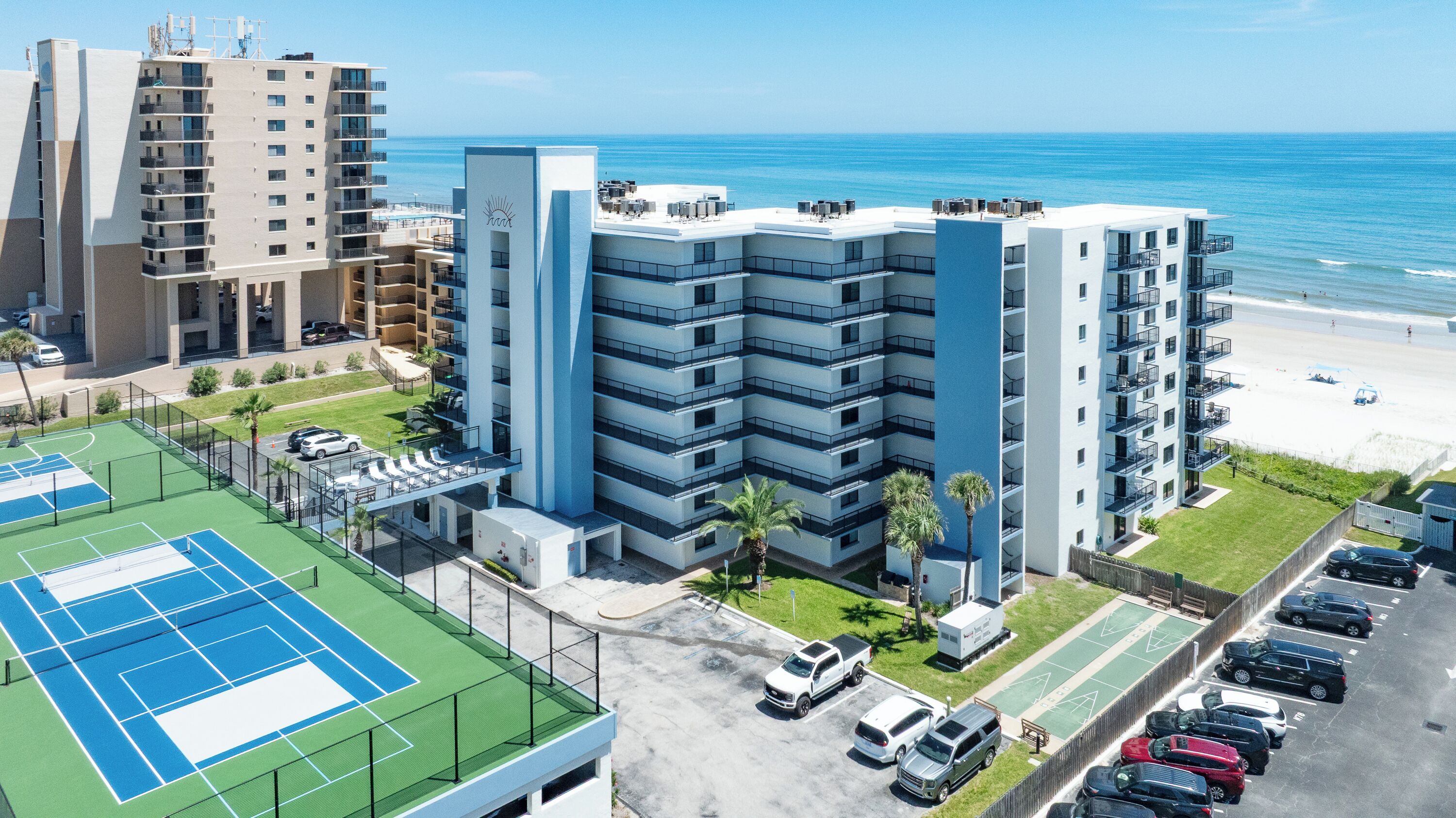 A multi-story hotel with a rooftop pool, tennis courts, and a parking area.