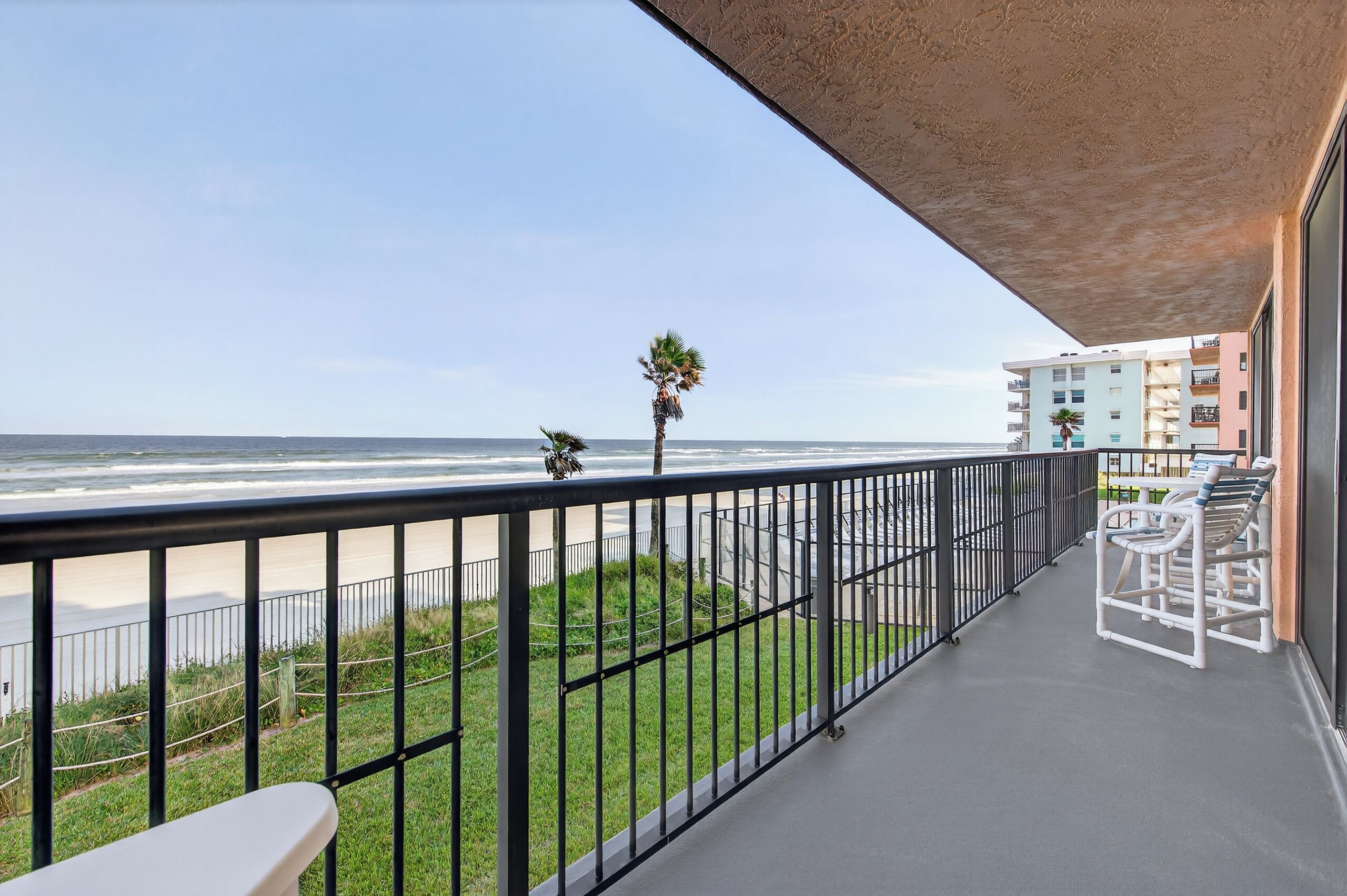 A balcony with a view of the ocean, a palm tree, and a building in the background.