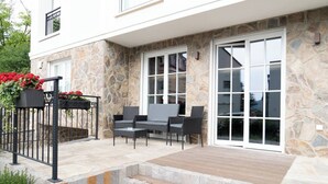 Un espace patio avec des murs en pierre, un ensemble de meubles d’extérieur et un portail orné de fleurs rouges.