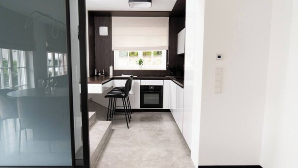 Une cuisine moderne avec un coin repas, un four encastré et une fenêtre donnant sur un espace verdoyant.