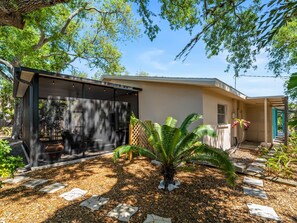 A house with a covered outdoor area, a small garden with a palm tree, and a pathway leading to the entrance. - Beach Access + Community Dock | Coastal Retreat (Englewood)
