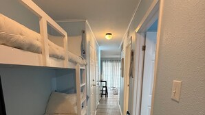 Un pasillo estrecho con literas a un lado y una puerta que da a otra habitación al otro.