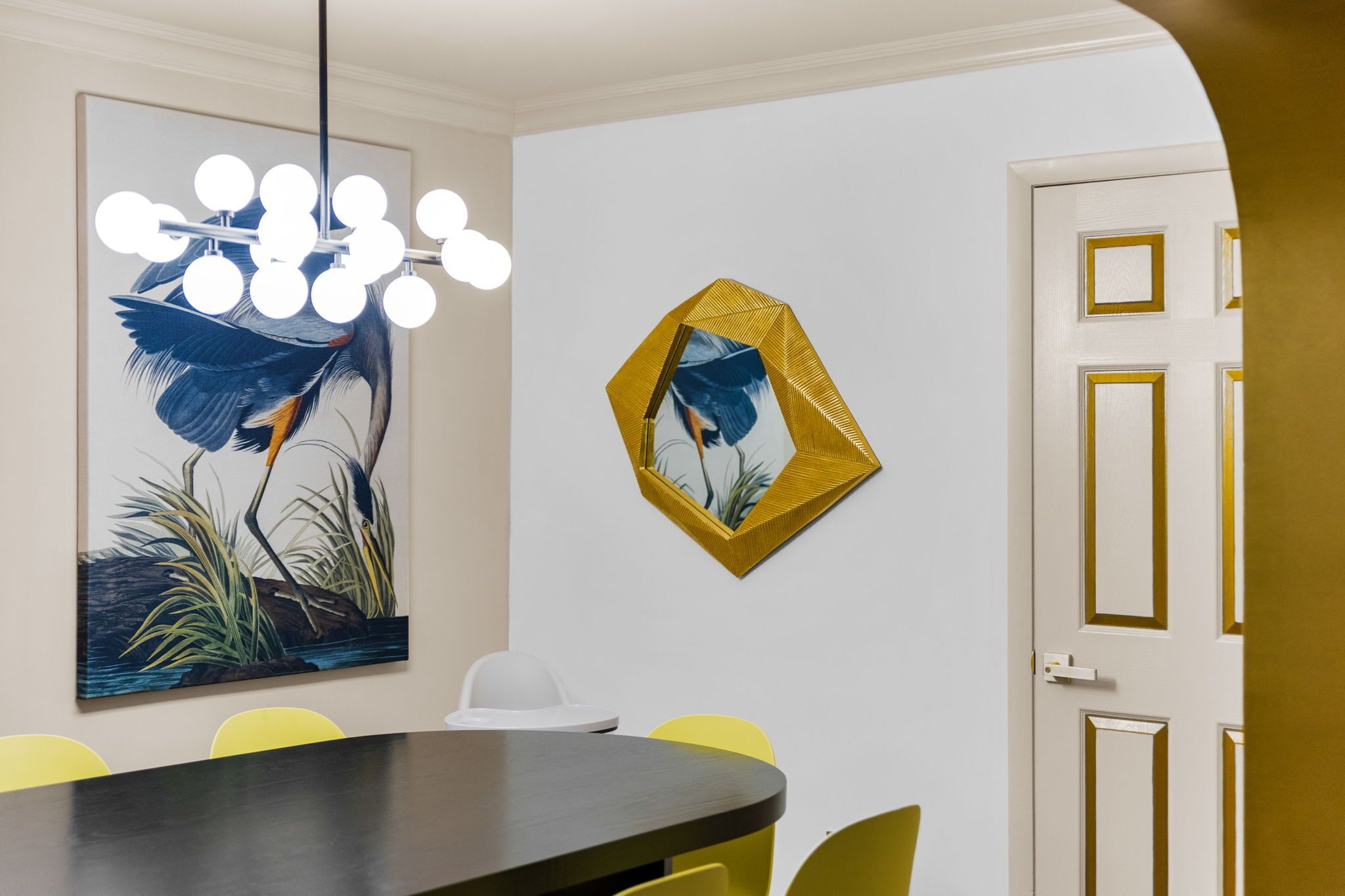 A dining area with a round table, yellow chairs, a chandelier, and wall art.