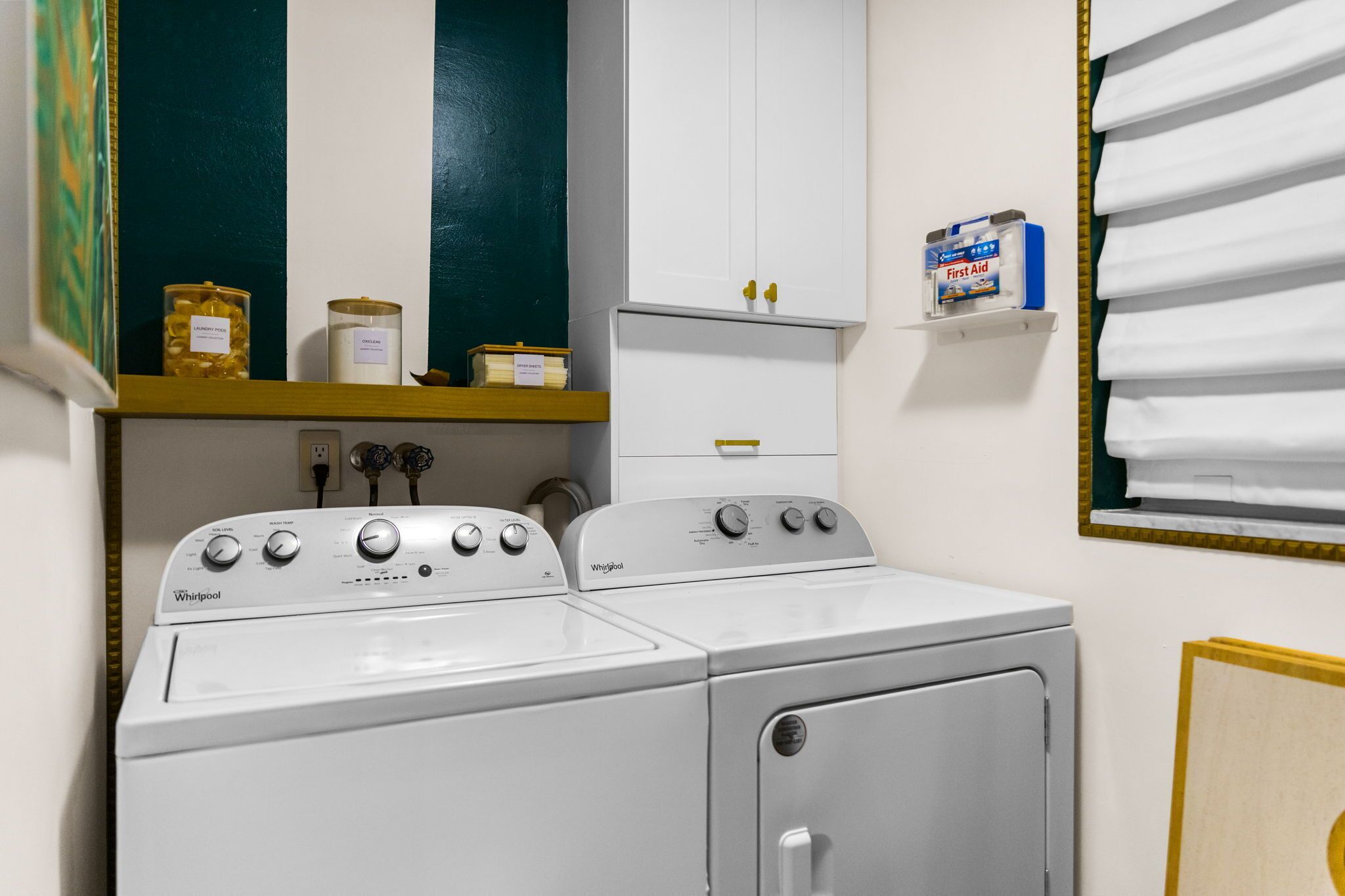 Un cuarto de lavandería con dos lavadoras y secadoras Whirlpool, un estante con artículos de tocador y un botiquín de primeros auxilios.