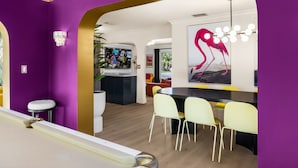Ein modernes Interieur mit einer violetten Wand, einer Bar mit gelben Stühlen und einem Essbereich mit einem schwarzen Tisch.