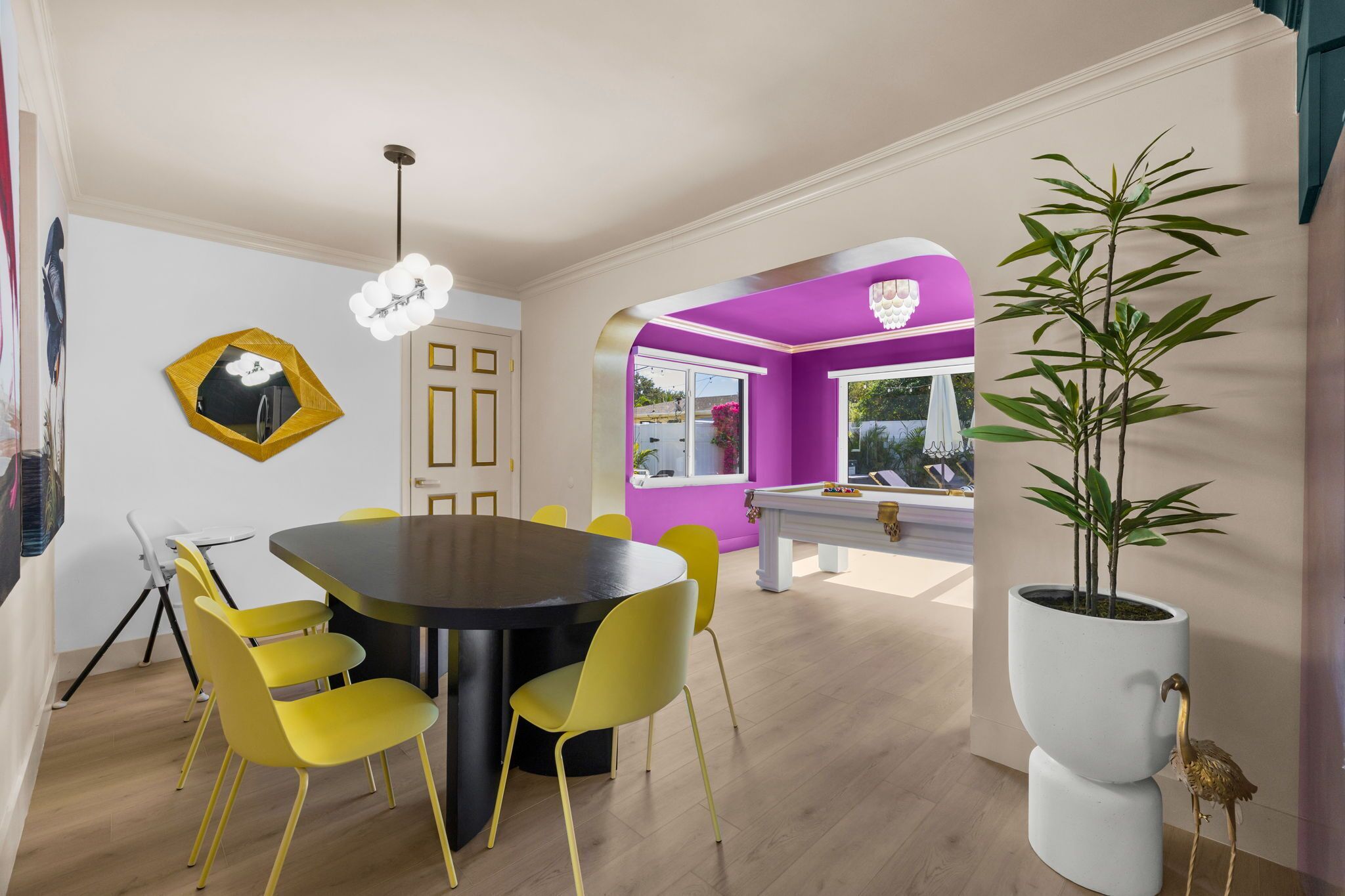 Un coin repas avec une table ronde et des chaises jaunes, une grande plante en pot et un mur d’accent de couleur violette.