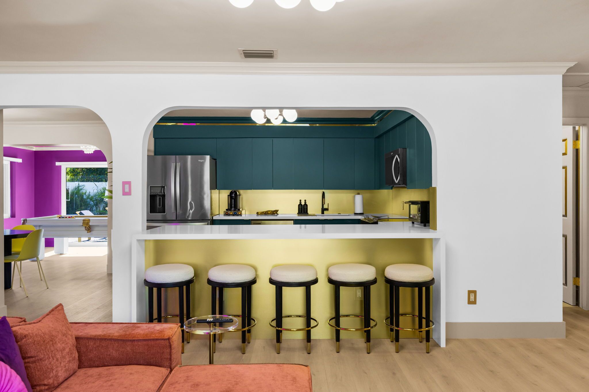 A modern kitchen with a central island, bar stools, and a pool table in the adjacent room.