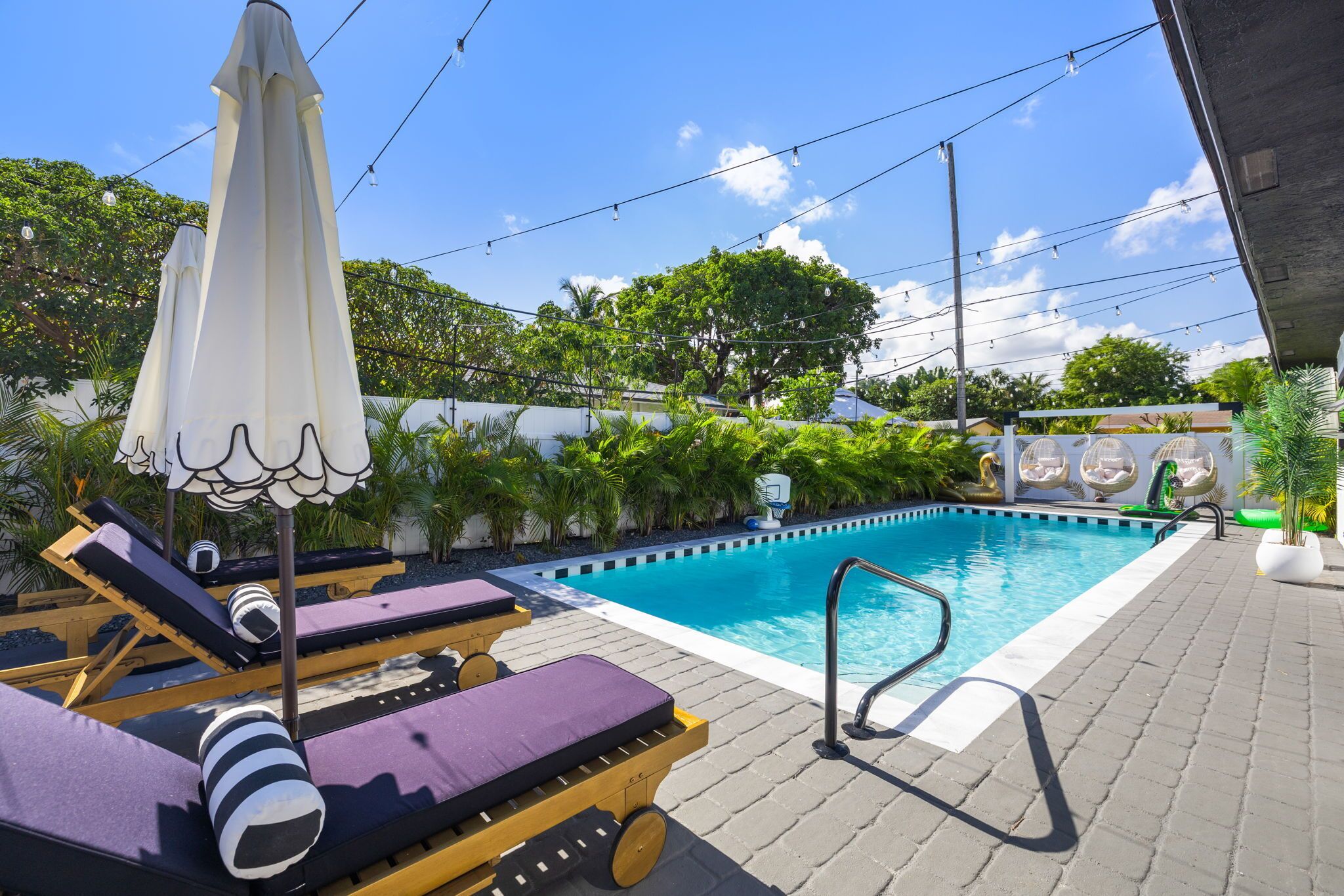 A pool area with lounge chairs, umbrellas, and a basketball hoop.