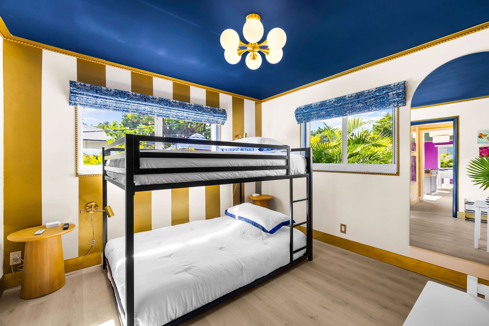 A bunk bed room with a ceiling fan, a small round table, and a window with a view of greenery.